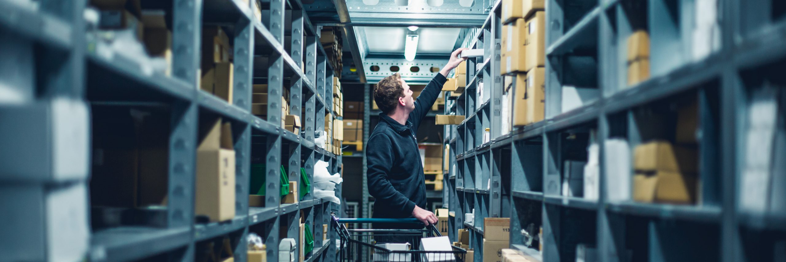 Young man employee GMs Instruments orderpicking product from shelf.